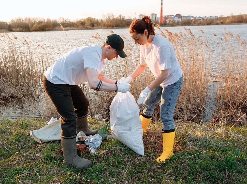 A young man and young woman in wellingtons picking up litter from beside a lake